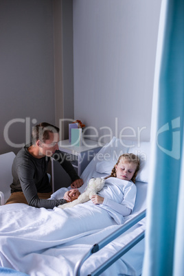 Father sitting beside her daughter lying on a hospital bed