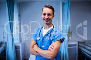 Portrait of male doctor standing with arms crossed in ward