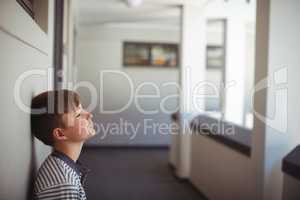 Sad schoolboy leaning head against wall in corridor