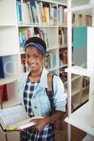 Portrait of happy schoolgirl holding book in library