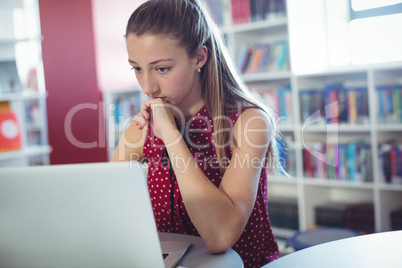Attentive schoolgirl using laptop in library
