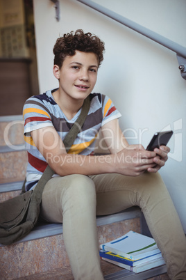 Portrait of schoolboy sitting on staircase and using mobile phone