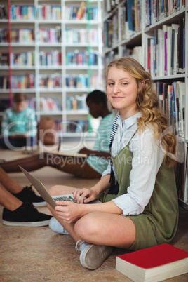 Portrait of happy schoolgirl using laptop in library