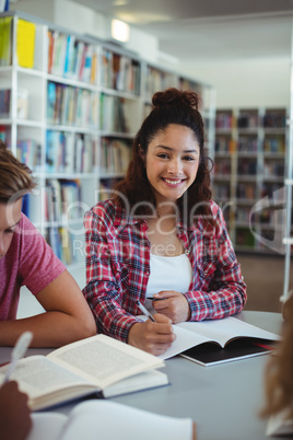 Portrait of happy schoolgirl studying with his classmates in library