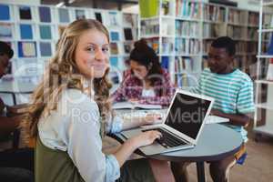 Smiling schoolgirl using laptop with her classmates studying in background