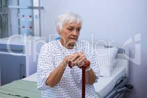 Worried senior patient sitting on bed with walking stick