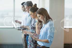 Business colleagues standing in a row using mobile phone, digital tablet and laptop