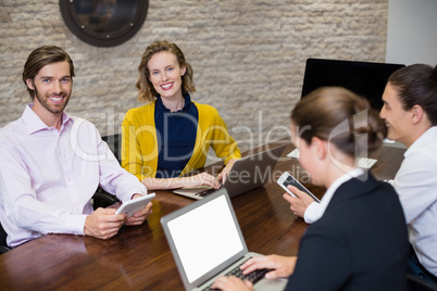 Business executives smiling while using electronic devices on conference table