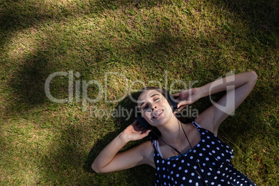 Woman lying on grass and listening to music with headphones