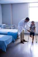 Doctor assisting injured boy to walk with crutches