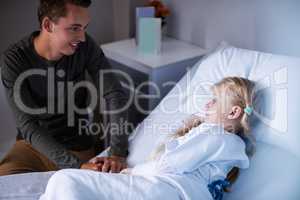 Father sitting beside her daughter lying on a hospital bed