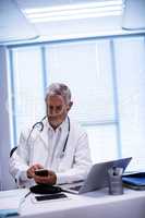 Doctor sitting at tablet and using mobile phone