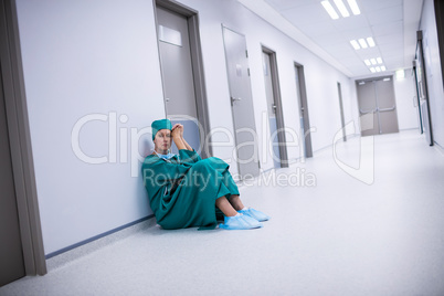 Tensed female surgeon sitting in corridor