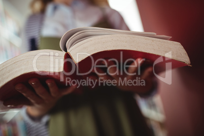 Mid-section of schoolgirl reading book in library