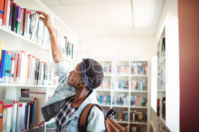 Schoolgirl selecting book from book shelf in library