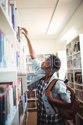 Schoolgirl selecting book from book shelf in library