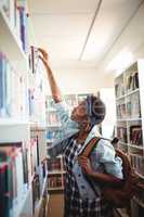 Schoolgirl selecting book from book shelf in library