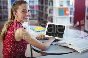 Portrait of happy schoolgirl using laptop in library