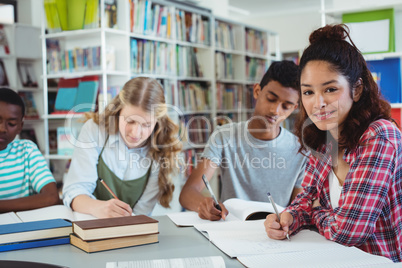 Portrait of happy schoolgirl studying with her classmates in library