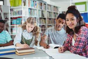 Portrait of happy schoolgirl studying with her classmates in library