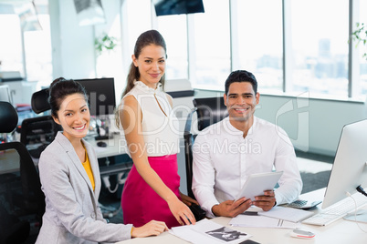 Smiling business colleagues discussing over digital tablet at desk in office