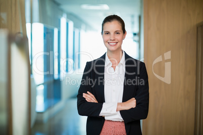 Smiling female business executive standing with arms crossed in corridor