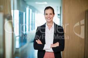 Smiling female business executive standing with arms crossed in corridor