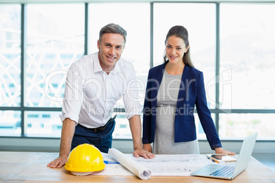 Smiling three architects standing in office with blueprint and laptop on table