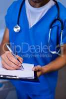 Mid section of nurse writing on clipboard in ward
