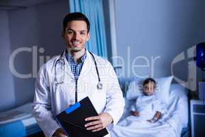 Portrait of male doctor standing with clipboard in ward