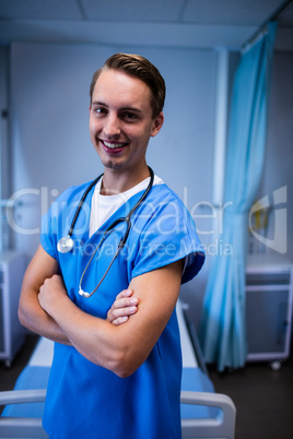 Portrait of male doctor standing with arms crossed in ward