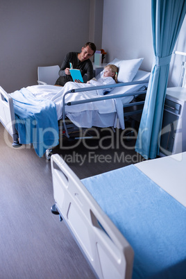 Girl on a hospital bed reading book with her father