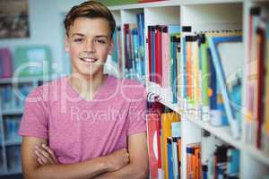 Portrait of happy schoolboy standing with arms crossed in library