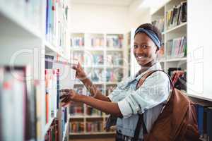 Schoolgirl selecting book from book shelf in library at school