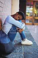 Portrait of sad schoolgirl sitting against brick wall