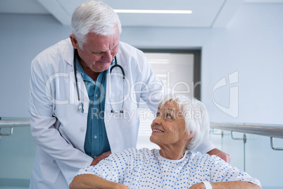 Doctor holding senior patient on wheelchair in passageway