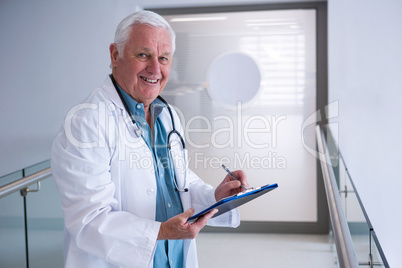 Doctor writing on clipboard in the passageway at hospital
