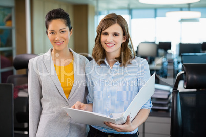 Smiling business colleagues discussing over clipboard at desk in office