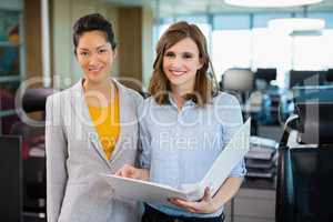 Smiling business colleagues discussing over clipboard at desk in office