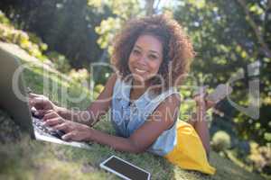 Smiling woman lying on grass and using laptop