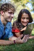 Couple lying on grass and using digital tablet