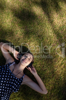 Woman lying on grass and listening to music with headphones