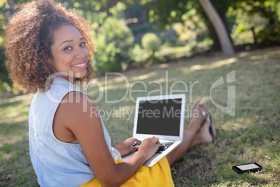 Smiling woman sitting in park and using laptop