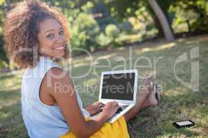 Smiling woman sitting in park and using laptop