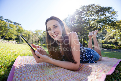 Smiling woman lying on mat and using digital tablet