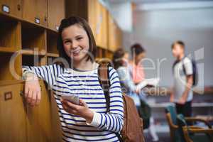 Portrait of happy schoolgirl holding mobile phone in locker room