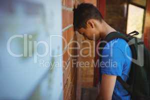 Sad schoolboy leaning on brick wall