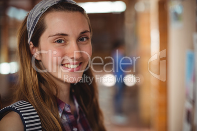 Portrait of smiling schoolgirl standing near notice board in corridor