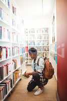 Schoolgirl selecting book from book shelf in library