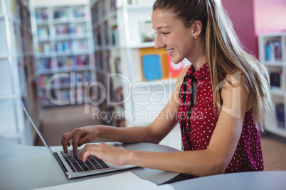 Happy schoolgirl using laptop in library